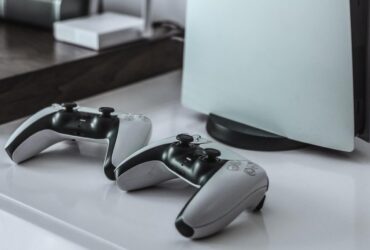 Dwa kontrolery DualSense na stoliku obok konsoli PlayStation 5