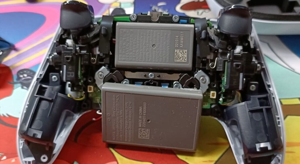Rozłożony kontroler DualSense Edge z widoczną baterią i baterią z DualSense dla porównania