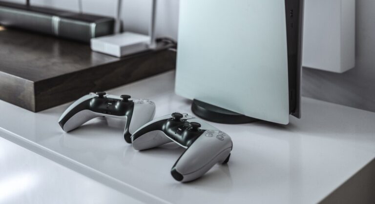 Dwa kontrolery od PlayStation 5 obok konsoli przy telewizorze