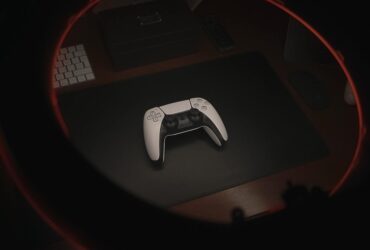 Biały kontroler od PlayStation 5 leżący na czarnym biurku