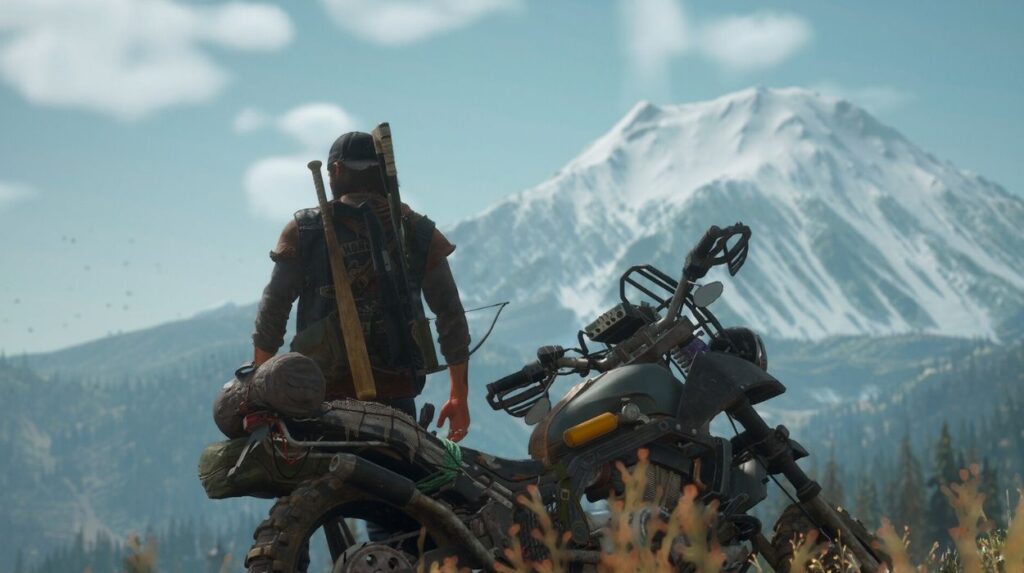Główny bohater Days Gone stoi przed motocyklem i patrzy na górską panoramę